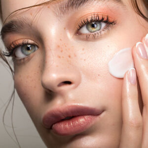 Intense Brigth Glow Treatment | HopeCosmetics Modern und bunt geschminkte junge Frau mit Sommersprossen stricht sich wenig Creme ins Gesicht