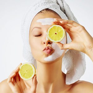 Junge Frau mit Kussmund und Creme im Gesicht hält Zitronenscheiben vor das Gesicht