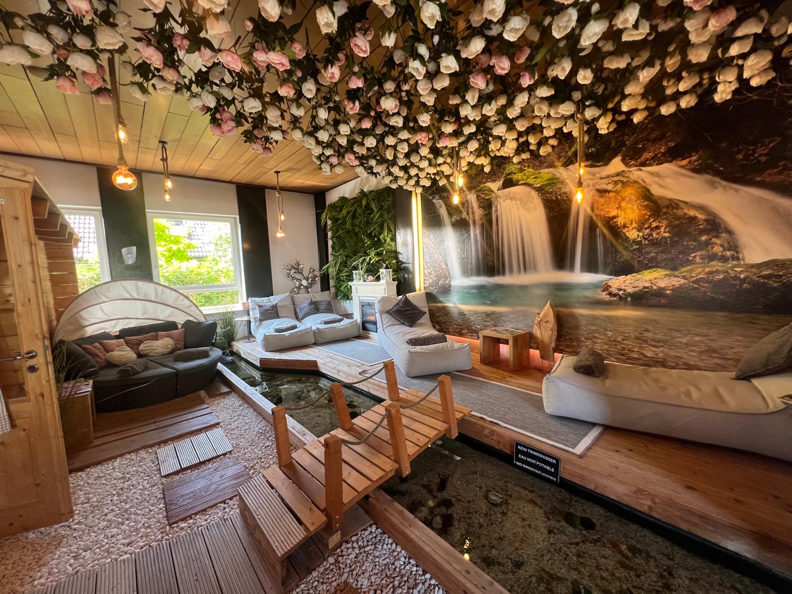 Ruhiger Entspannungsbereich im HopeCosmetics DaySpa Nürnberg mit Blütenhimmel, Wasserlauf, Holzbrücken und alpiner Wellness-Atmosphäre