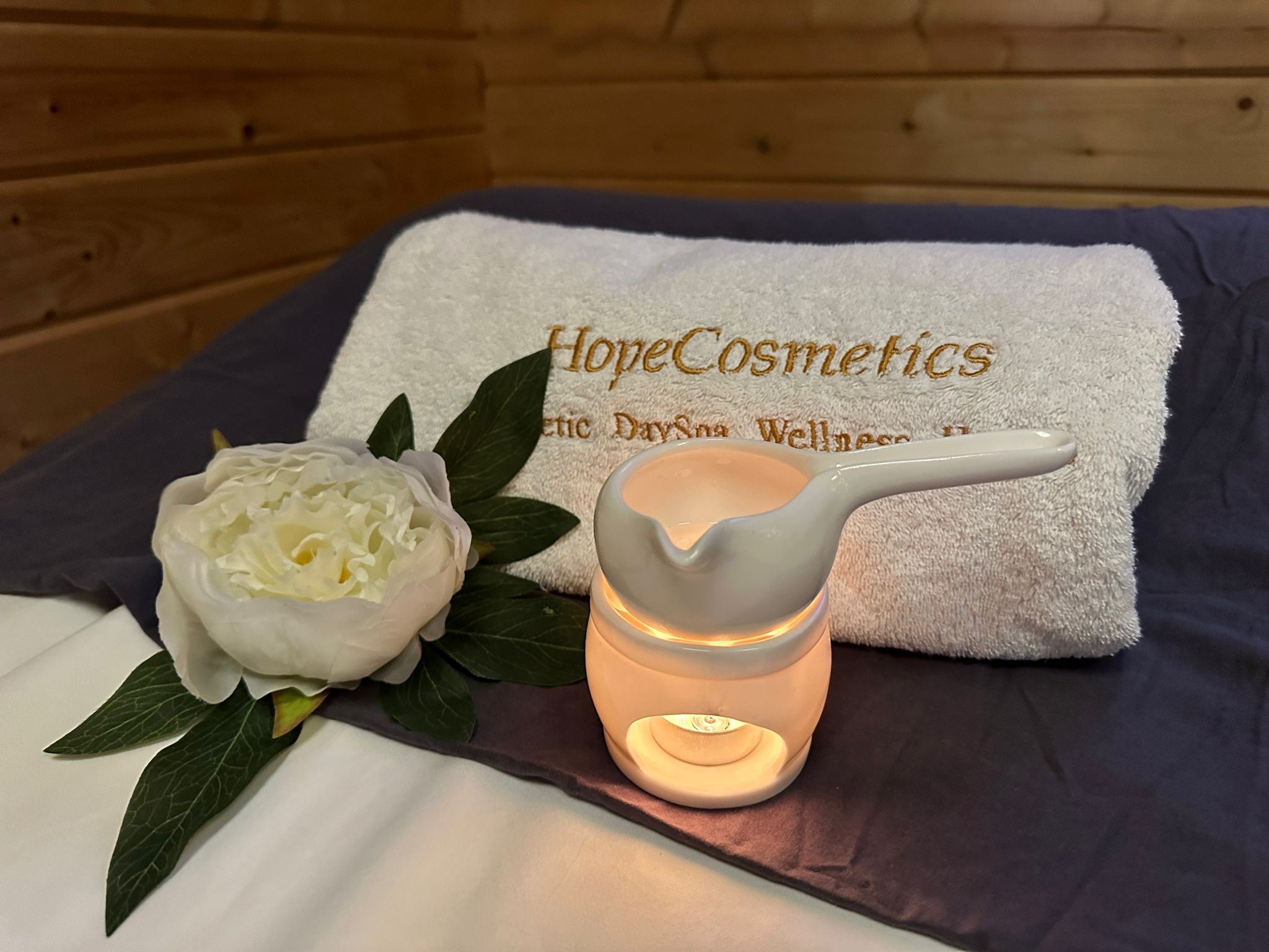Detailaufnahme im HopeCosmetics DaySpa Nürnberg mit besticktem Handtuch, warmer Duftlampe und Blüte für eine entspannende Wellness-Atmosphäre